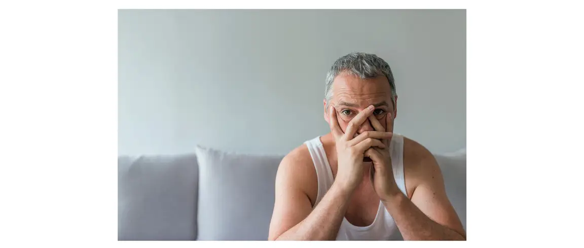 Man sitting on couch. He is resting his head in his hands. He looks frustrated.