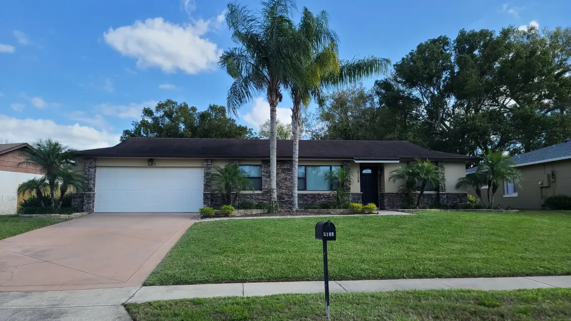 Well-maintained single-story home by Investment Capital Home Buyers, featuring a two-car garage, palm trees, and a green front yard – sell my house fast Orlando.