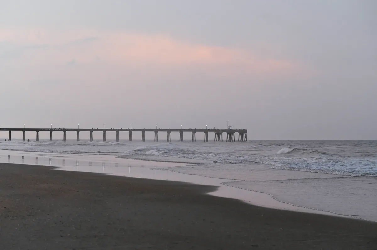 Surf City pier in silhouette over the beach at dusk in Surf City, North Carolina