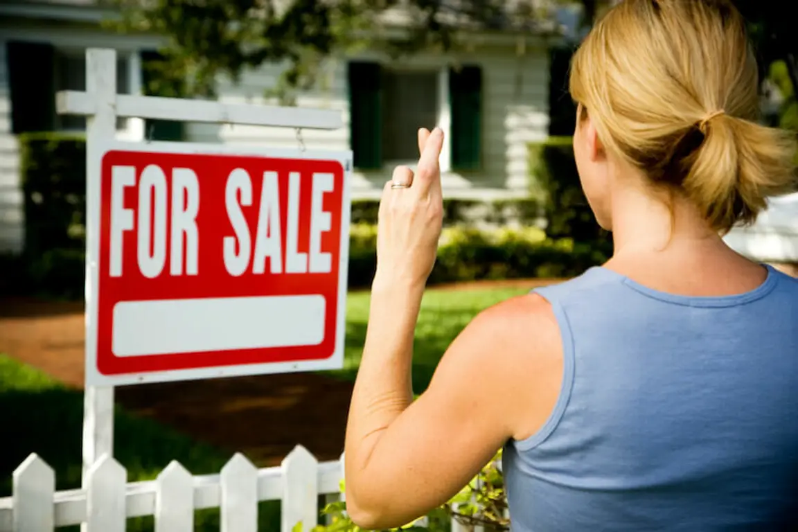 woman and for sale sign with house as background