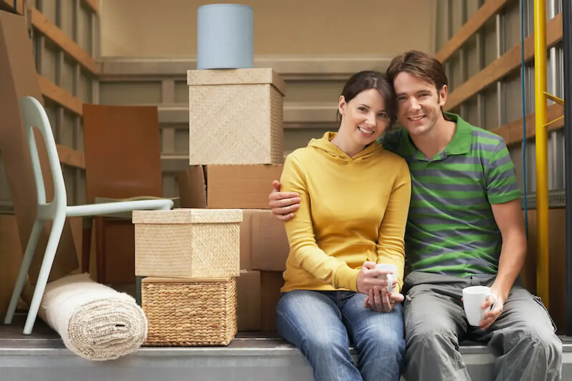 smiling young couple sitting back of a van moving out of state
