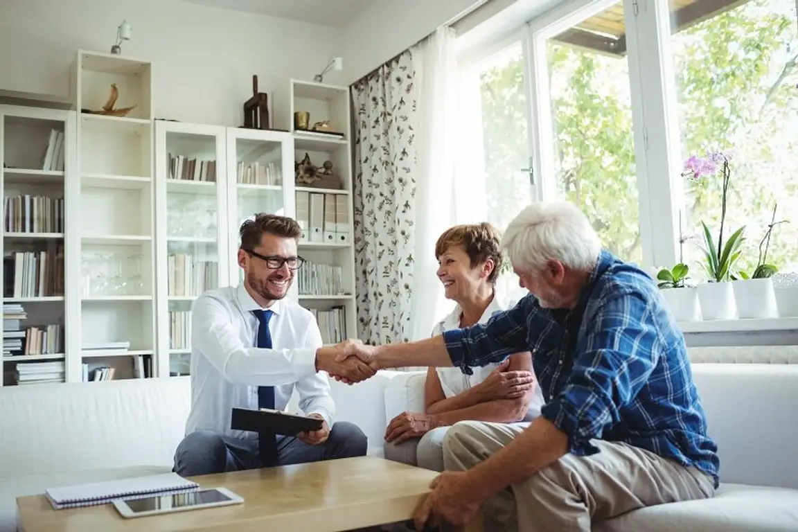A young home investor shakes hands with a couple of senior homeowners