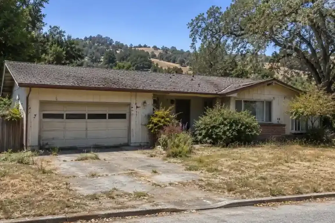 Sell my house fast in Sonoma CA fixer upper 1970s ranch home with deferred maintenance, aging roof, overgrown landscaping, and rolling Sonoma hills in the background.