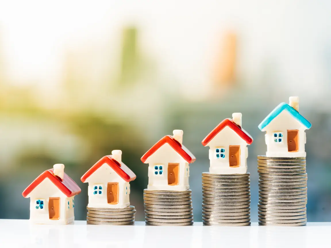 Real estate investment stock photo - house figurines on top of stacks of coins