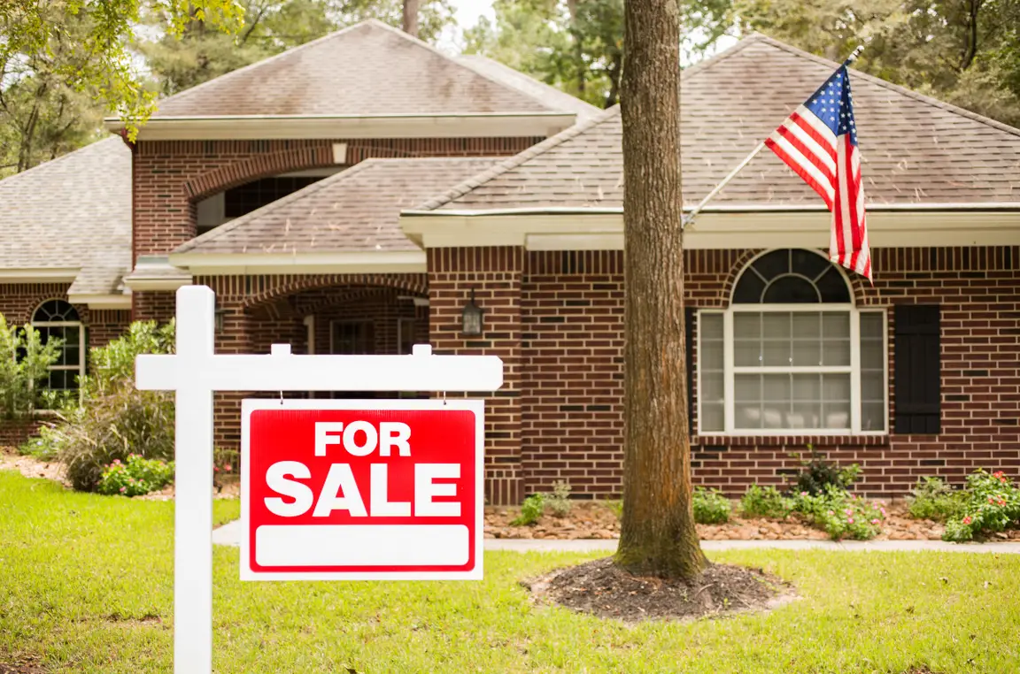 A house with a "For Sale" sign in the front yard