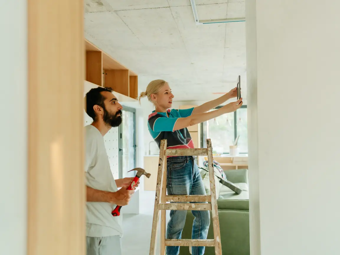 A man and a woman with a ladder and a hammer working on a home improvement project.