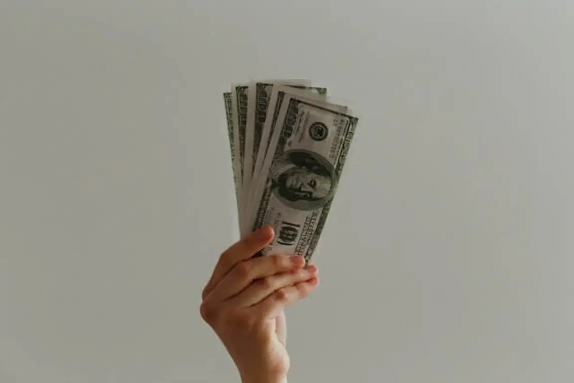 A person holding five hundred-dollar banknotes in one hand.