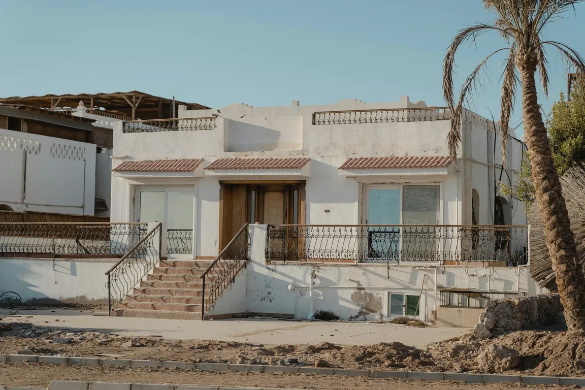 small white home with palm tree and dirt patch
