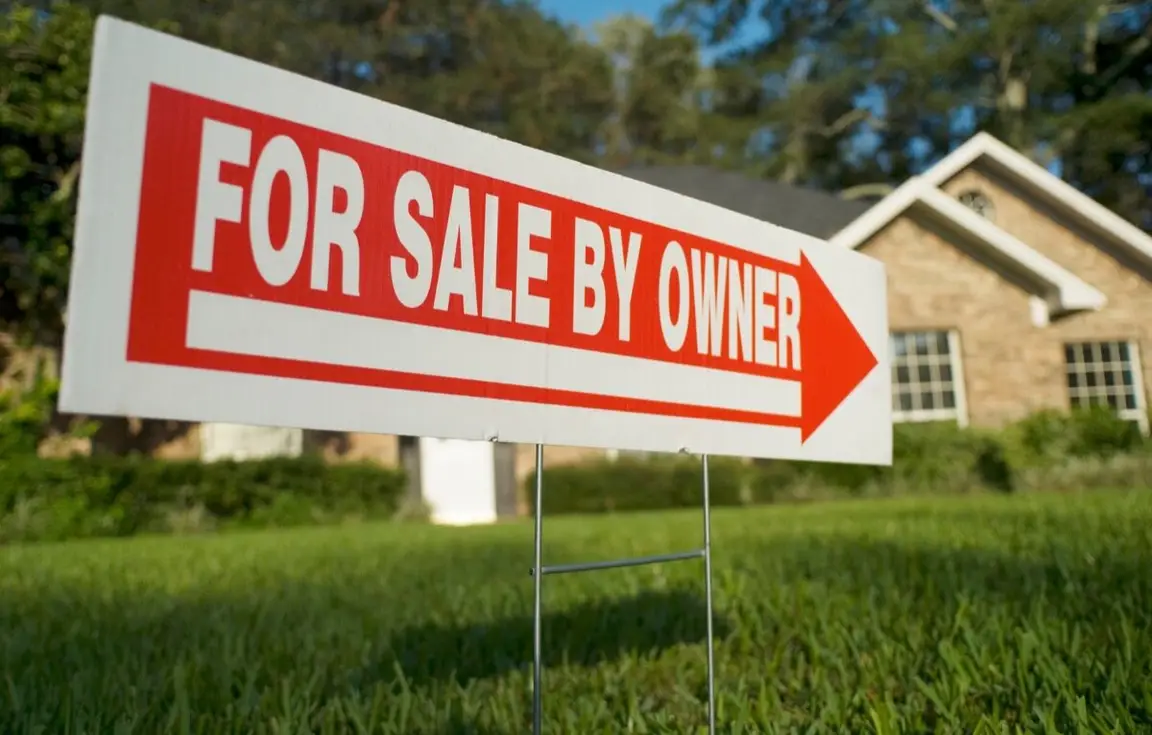 For sale by owner sign staked in the front yard of a house