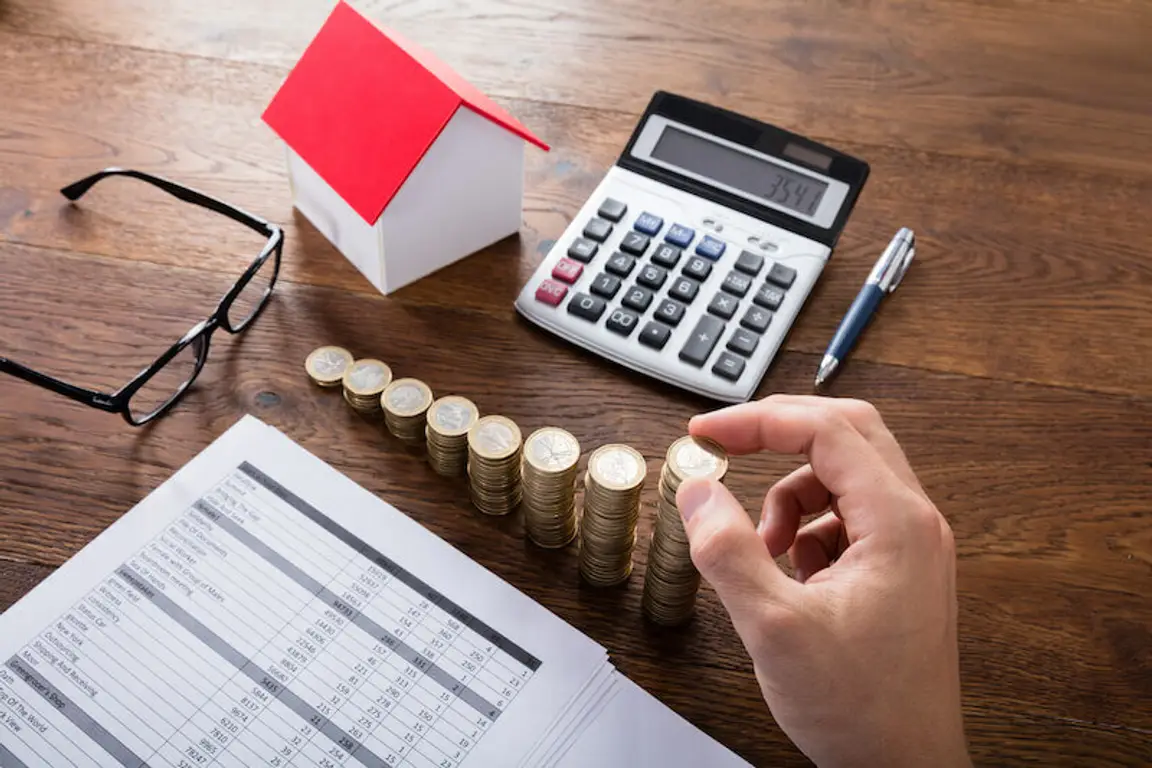 Person Liquidating hid assets - Stacking Coins Near House On Wooden Desk