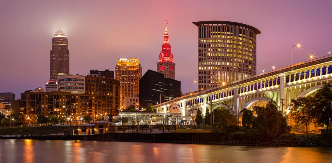 Downtown Cleveland skyline at dusk with illuminated skyscrapers and the brightly lit Veterans Memorial Bridge over The Cuyahoga River. This is the cover photo for Realty Done by Damien Baden's homepage – the best real estate agent to help you buy and sell homes in Northeast Ohio.