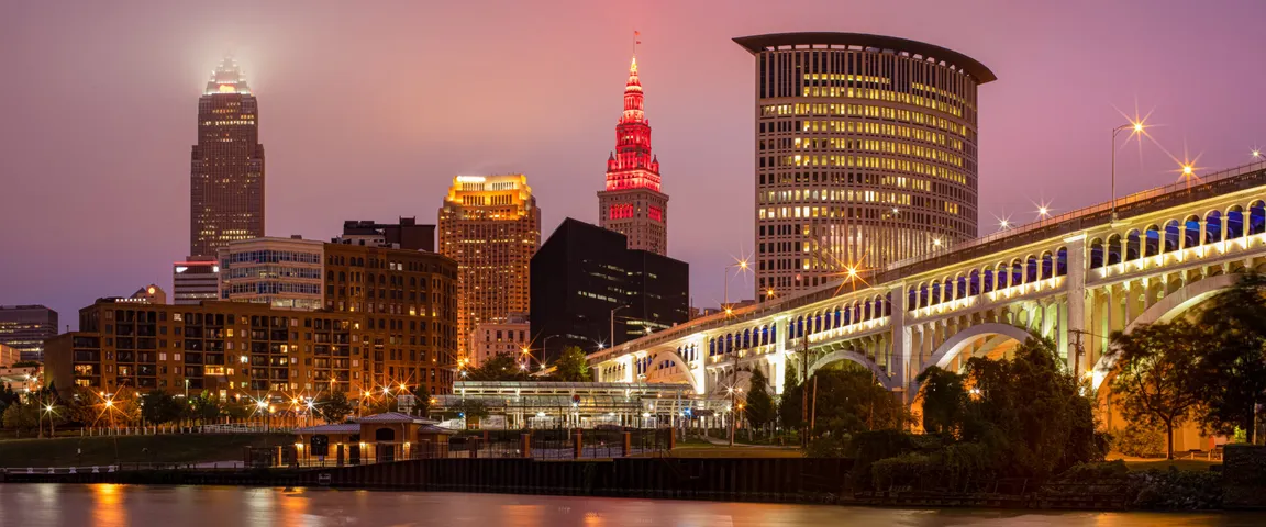 Downtown Cleveland skyline at dusk with illuminated skyscrapers and the brightly lit Veterans Memorial Bridge over The Cuyahoga River. This is the cover photo for Realty Done by Damien Baden's homepage – the best real estate agent to help you buy and sell homes in Northeast Ohio.