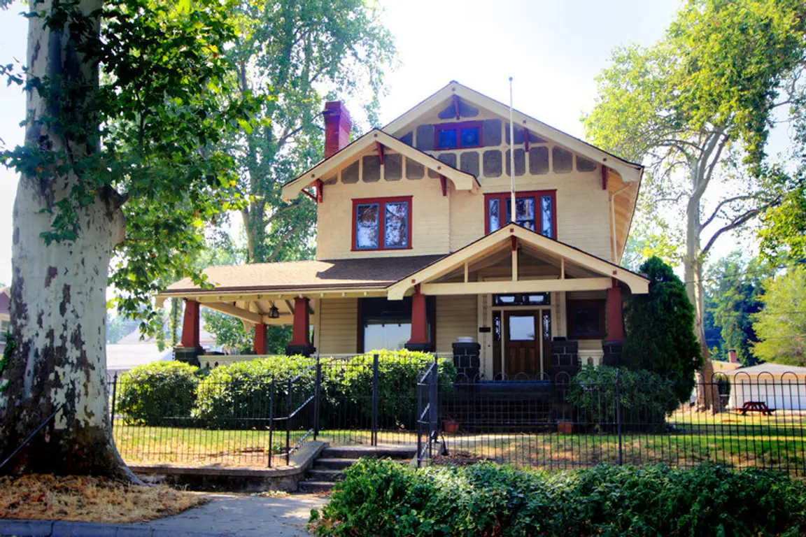large-two-story-tan-house-with-a-front-porch-and-a-large-tree-in-the-yard