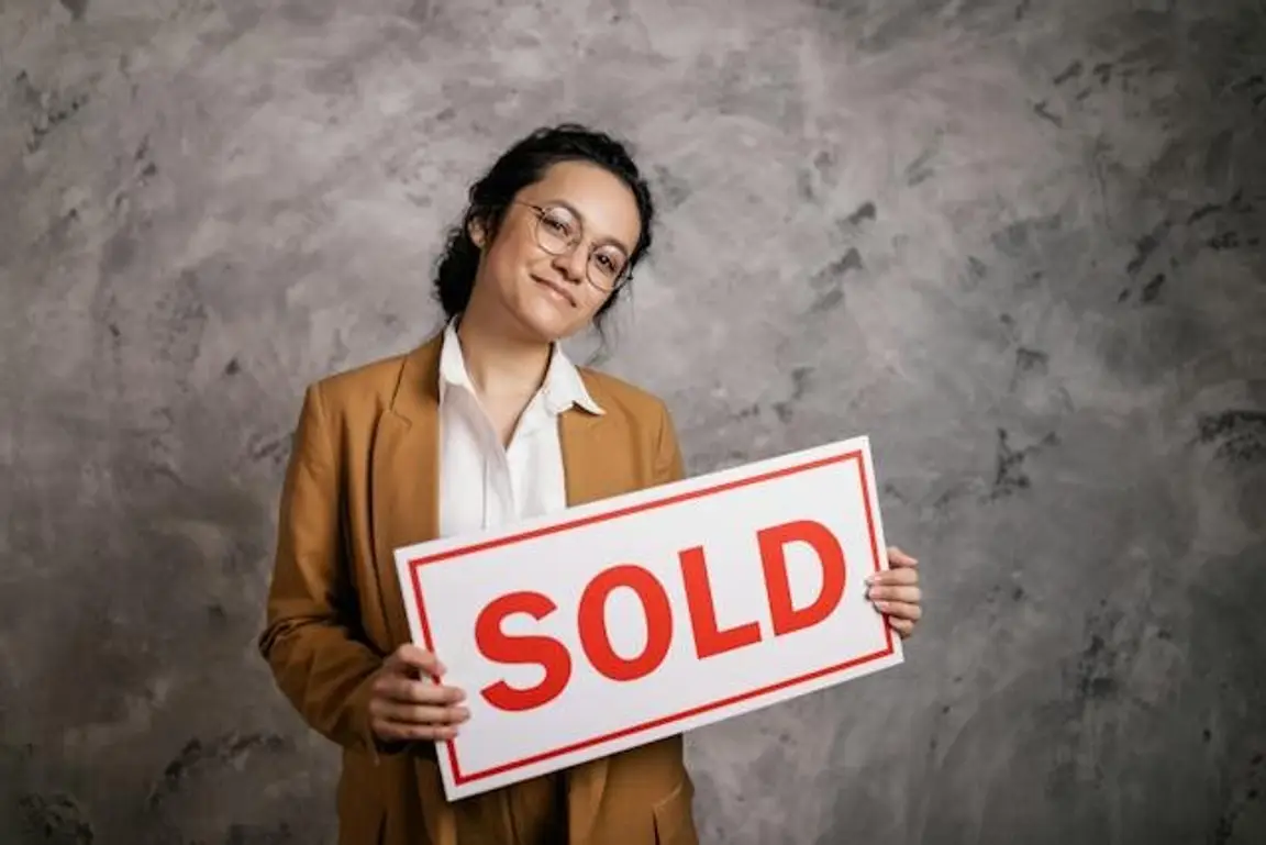 A woman with a brown blazer holding a sold sign