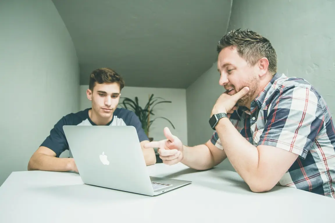 Two men with a laptop discussing the topic of choosing the right season to sell your home and move with a realtor