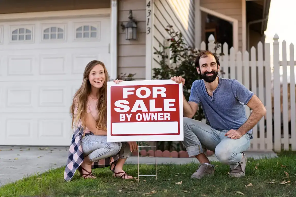 Man and woman posing with a for sale sign in front of their house