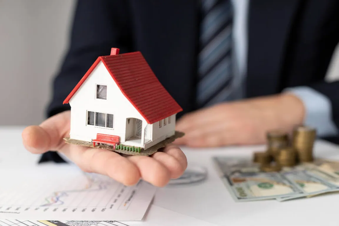 A man in suit holding a miniature house