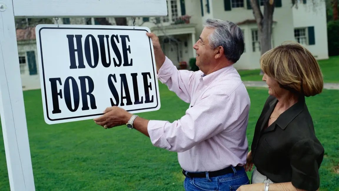 A couple holding a "House for Sale" signboard