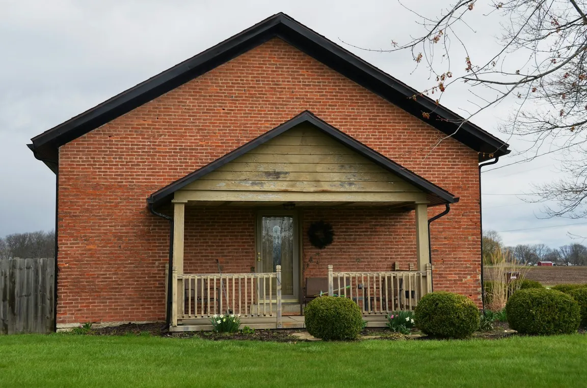 Older brick house with a covered front porch and a wooden fence