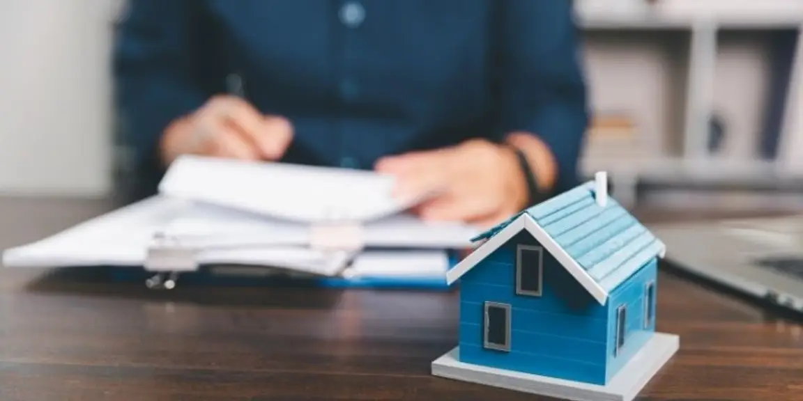 model house on desk with person reviewing financial documents in background