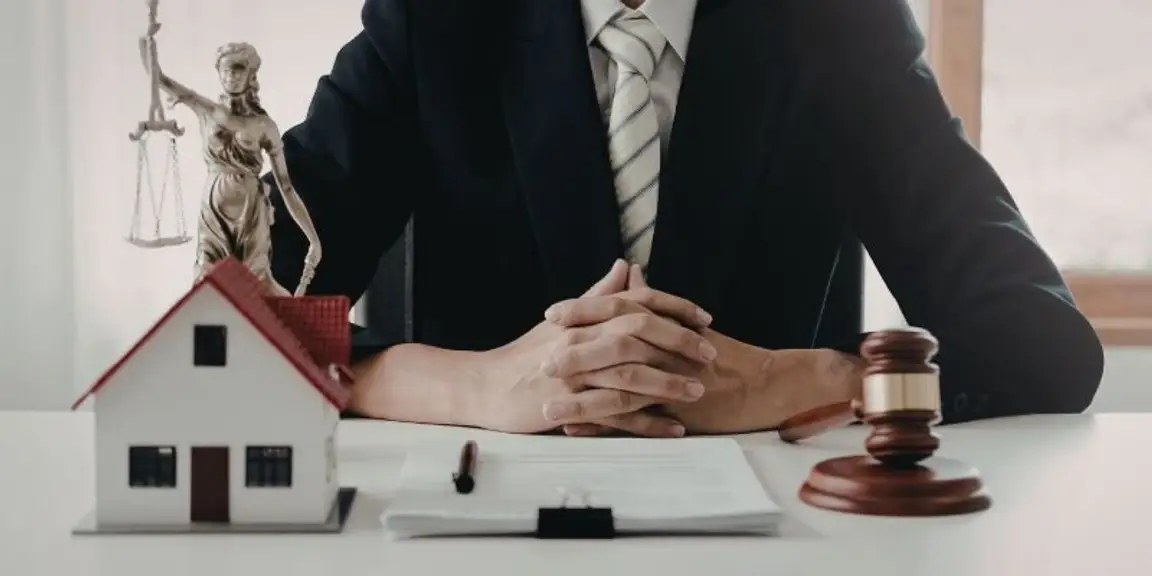 person in suit with gavel, model house, and scales of justice on desk