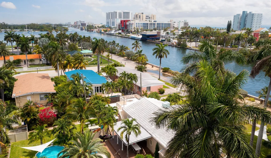 Arial view of a sunny Florida neighborhood with a waterfront property featuring a swimming pool, showcasing a prime real estate location for homeowners looking to sell my house fast.