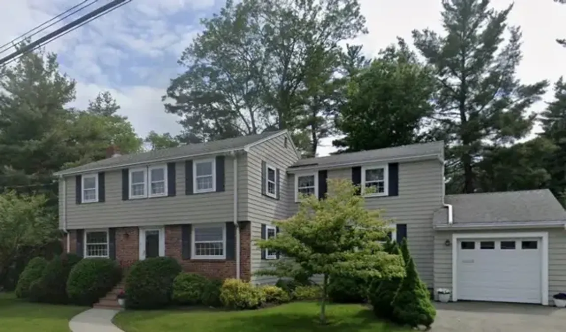 Front exterior view of a two-story residential house with side garage addition and mature landscaping