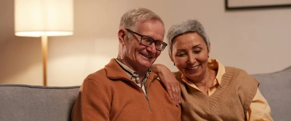 Smiling older couple sitting on a couch looking at a laptop together regarding Unclaimed Money Maryland Unclaimed Funds Surplus Funds