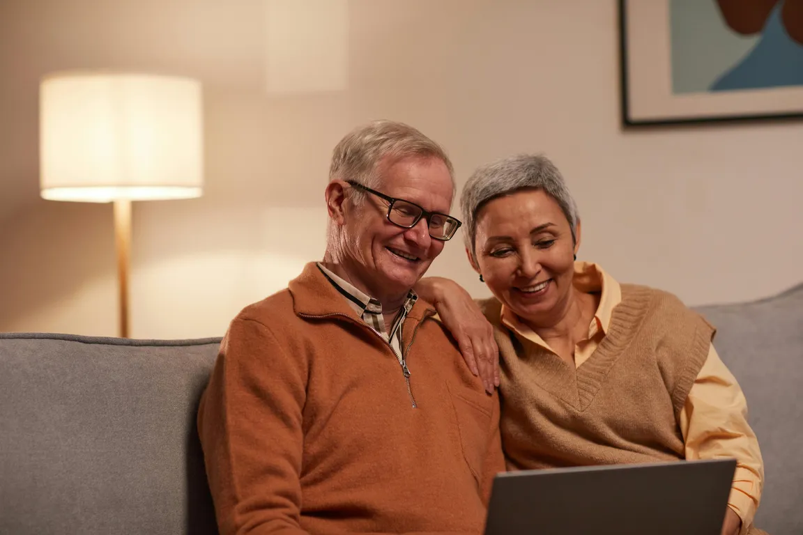 Smiling older couple sitting on a couch looking at a laptop together regarding Unclaimed Money Maryland Unclaimed Funds Surplus Funds