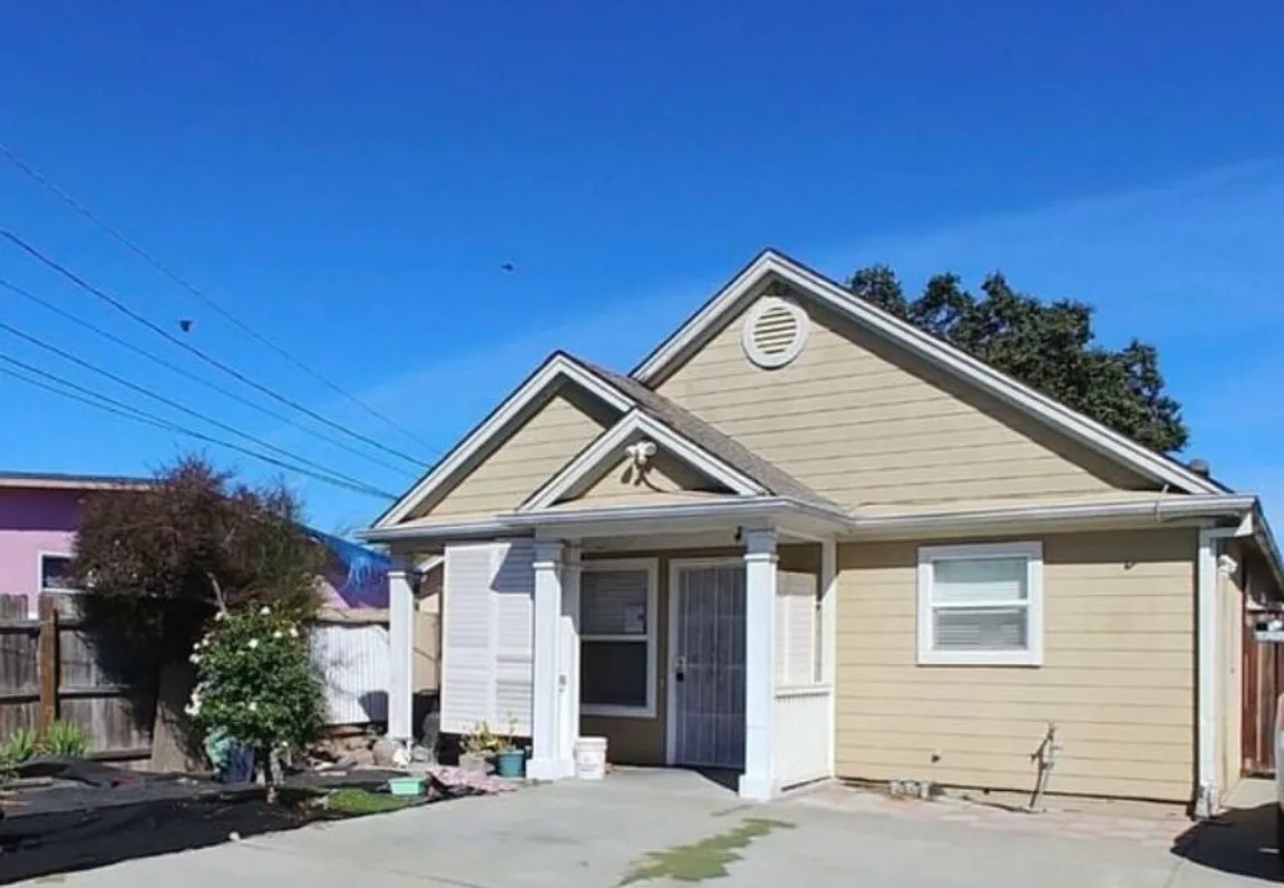 Single-story tan house with white trim and text overlay reading “Facing Foreclosure?” under a clear blue sky.