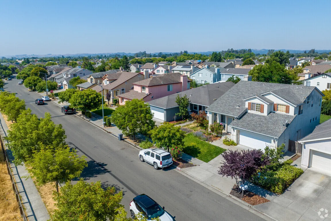 Aerial view of a quiet suburban neighborhood with tree-lined streets and modern two-story homes on a clear day.
