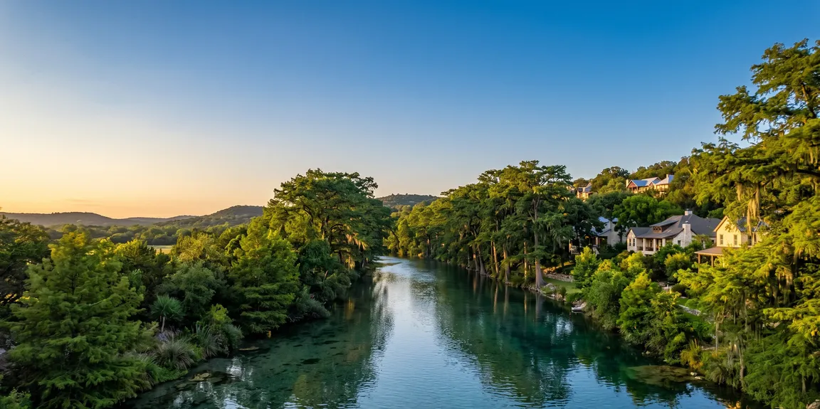 Scenic view of the Comal River or Guadalupe River landscape in New Braunfels Texas with homes nestled along the water at sunset, for New Braunfels cash home buyers.