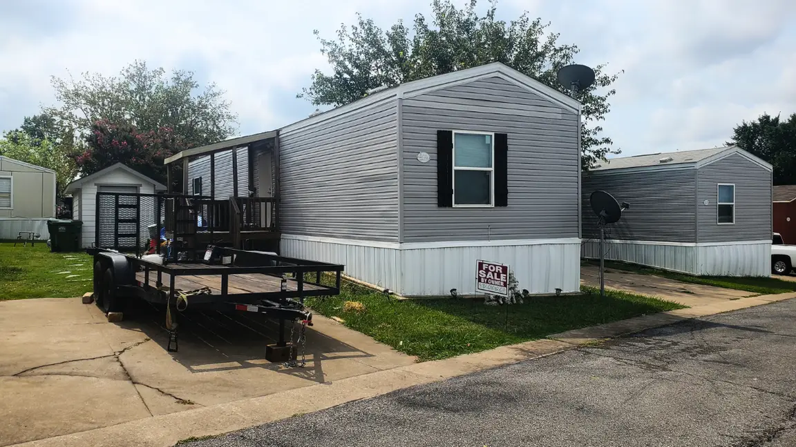 Flatbd trailer with two junk mobile homes in a park - we buy mobile homes as is!