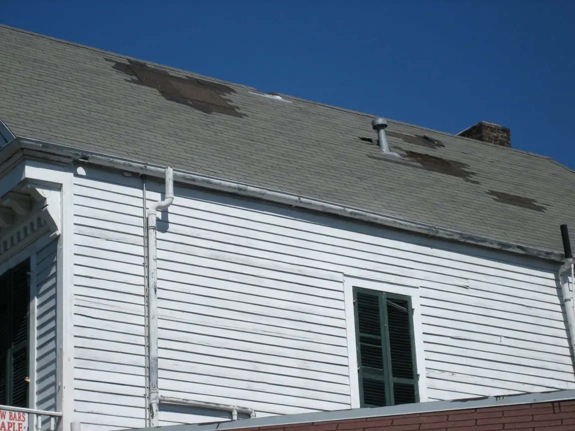 A white building that has wind damage causing a leaking roof.
