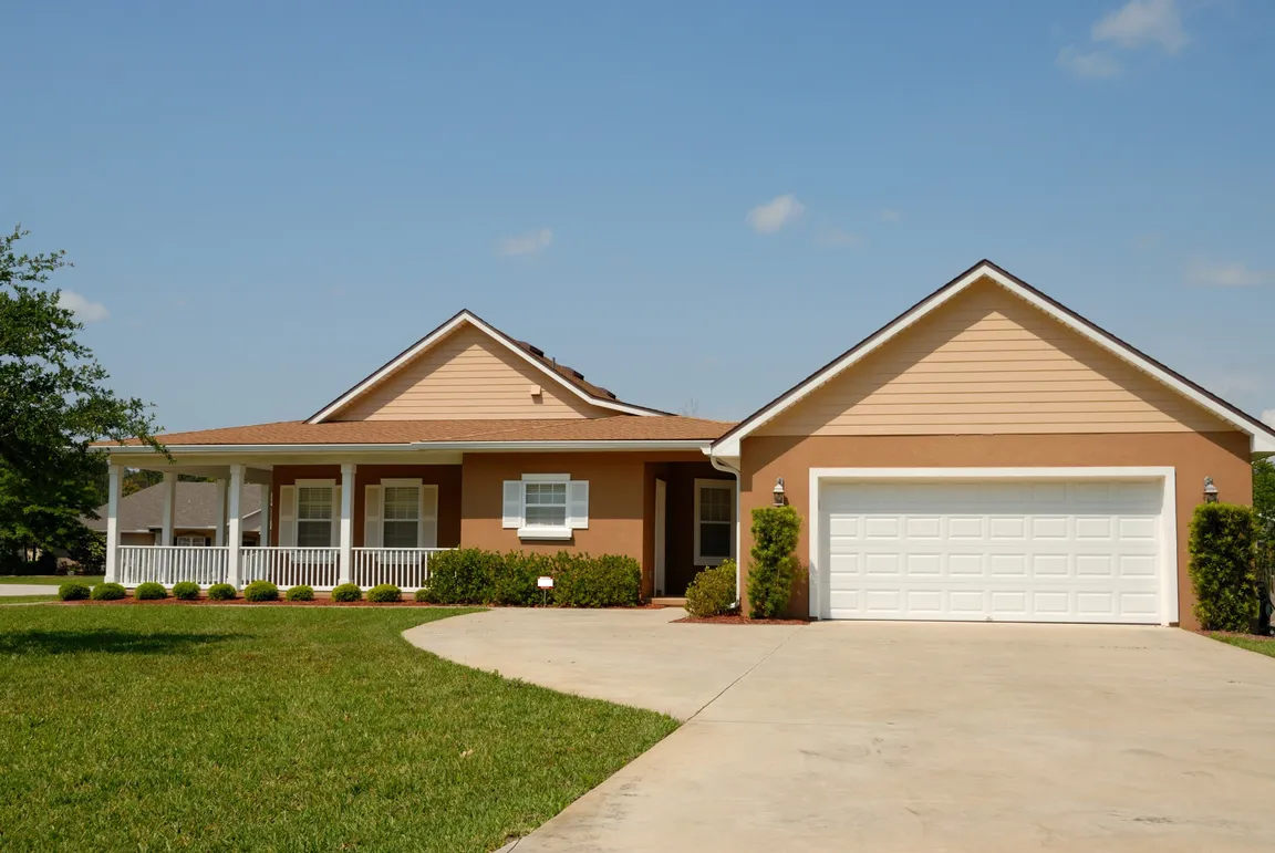 yellow ranch style home with 2 car garage and large paved driveway