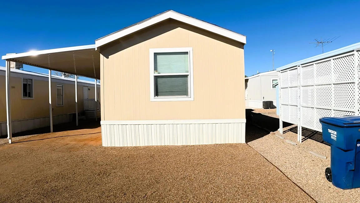 Single wide mobile home in Tucson community with covered carport and gravel yard
