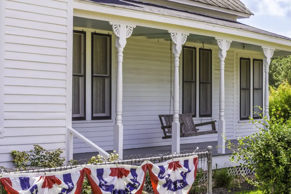Front view of a white house in Texas with a porch swing and flags hanging