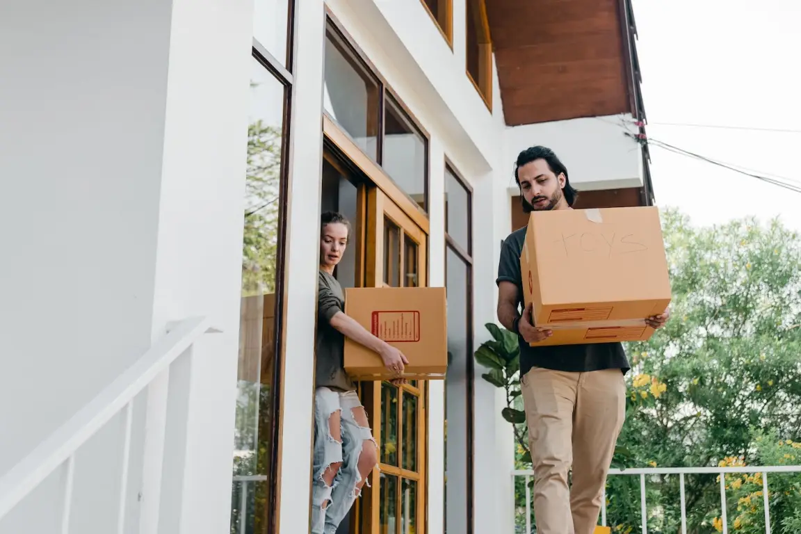 Two people carrying moving boxes out of a house