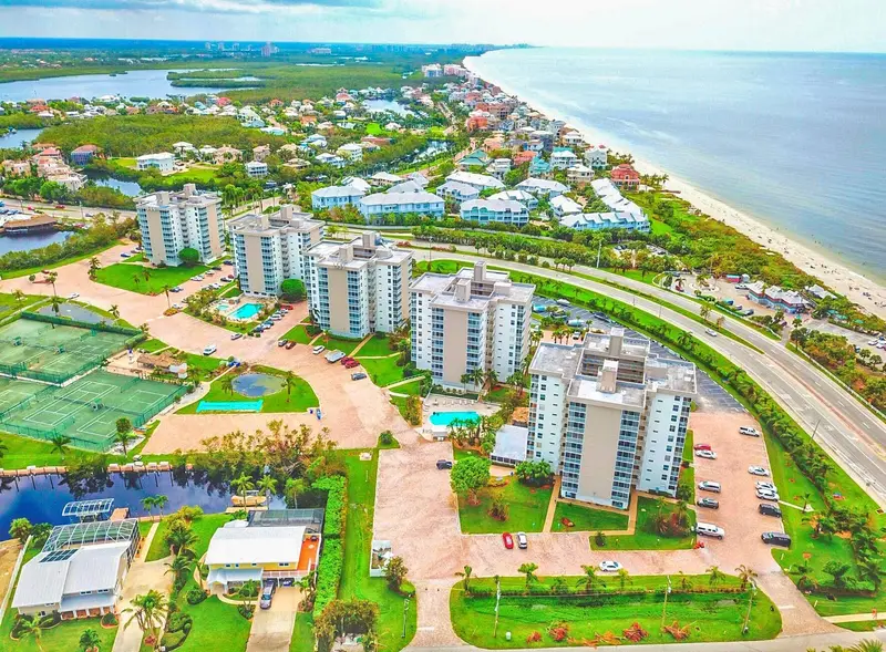 Aerial view of Beach and Tennis Club in Bonita Springs, with five mid-rise condominium towers, pools and tennis courts next to a beachfront road and the Gulf of Mexico