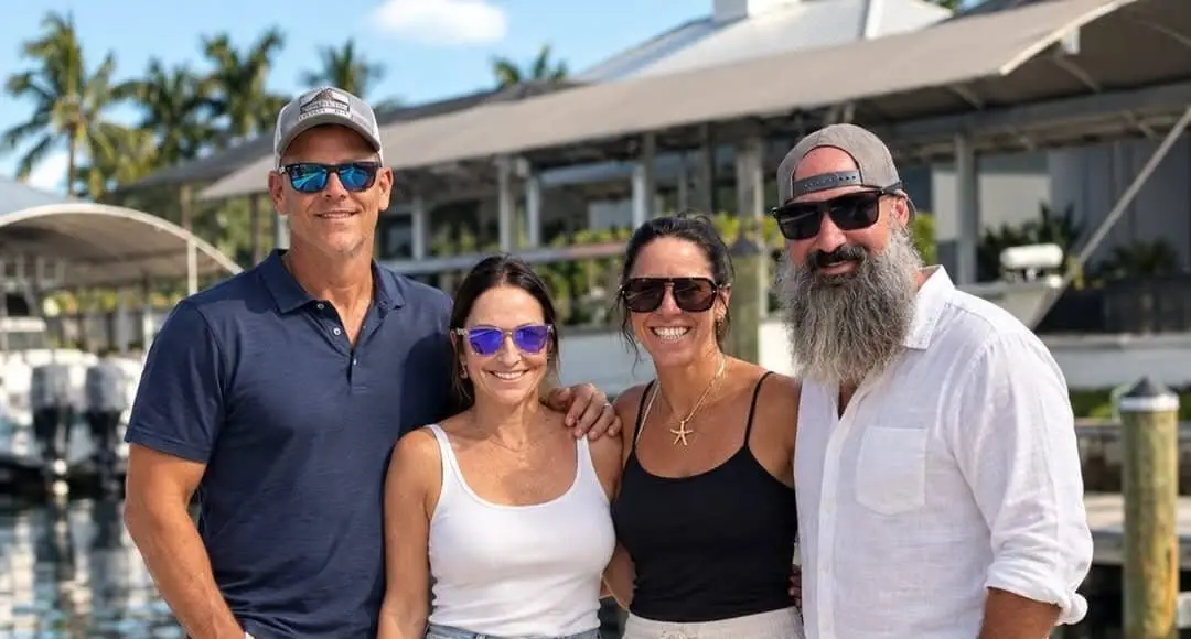 The SWFL Waterfront Collection real estate team, four people smiling together on a marina dock with boats and palm trees behind them