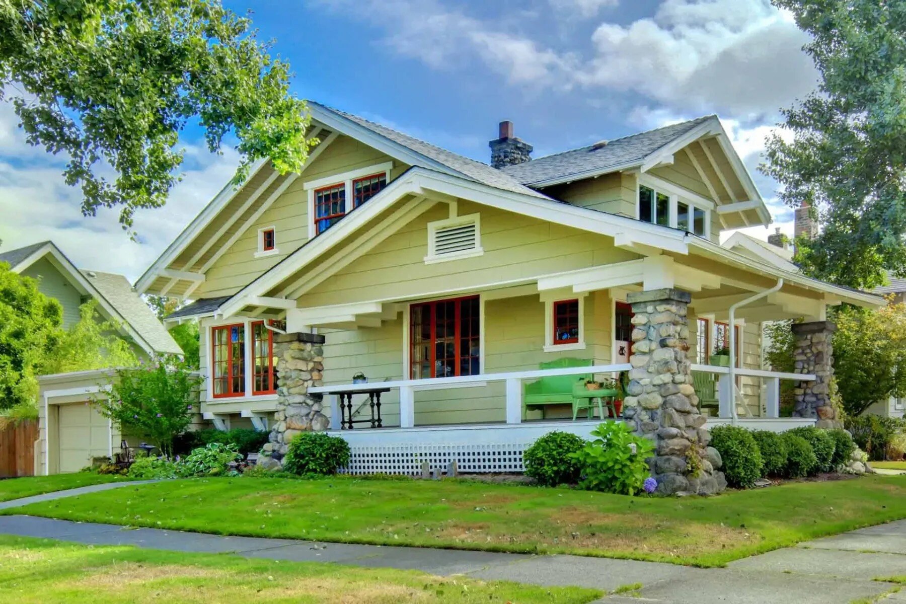 Sprawling yellow bungalow home on a corner lot with stone columns and greenery