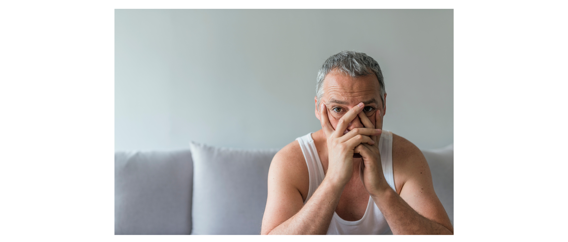 Man sitting on couch. He is resting his head in his hands. He looks frustrated.