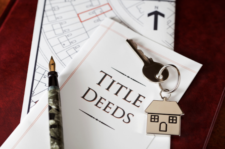 A writing pen and house key laying on a title deed to a home.