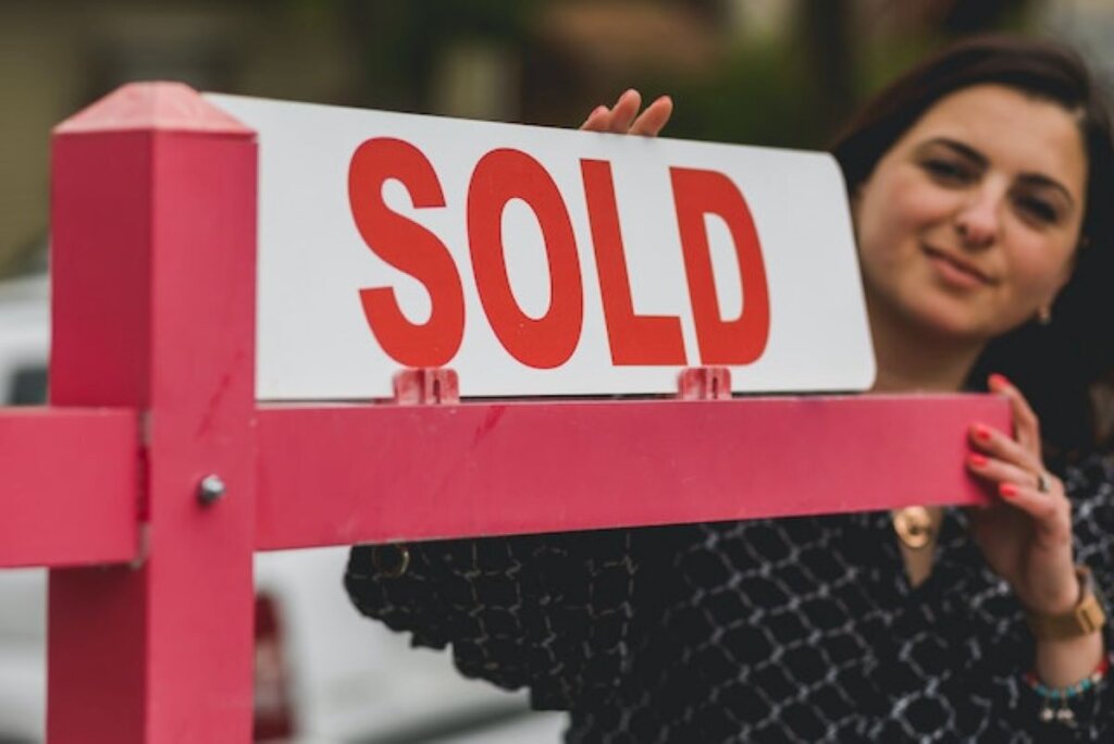 A woman next to a SOLD sign.
