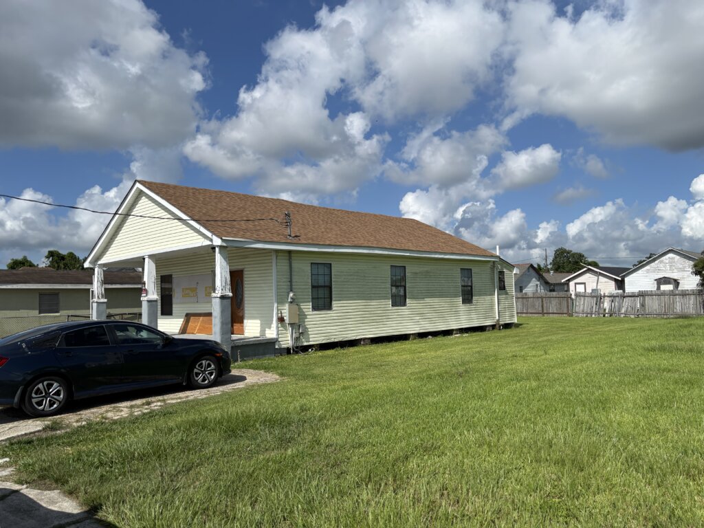 Exterior of an older house with missing vinyl siding and a patchy front lawn, potentially hiding termite damage beneath the surface