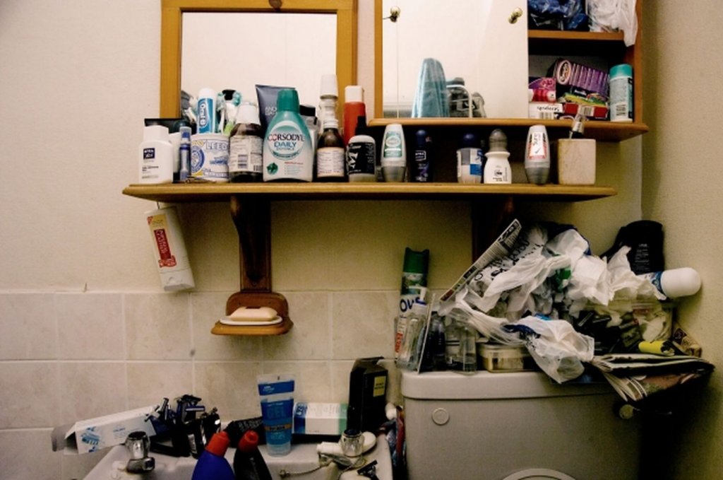 A bathroom with a lot of things stacked around in a hoarder house.