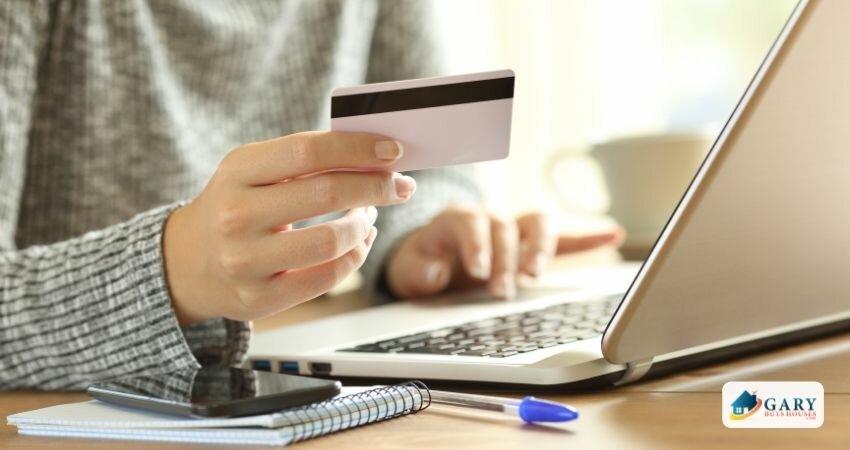 Woman holding a credit card and a laptop, phone and paper on a table.