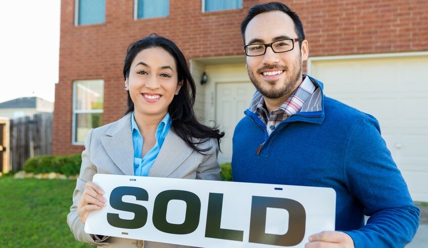 A man and a woman holding a sign that says SOLD in front of a house.