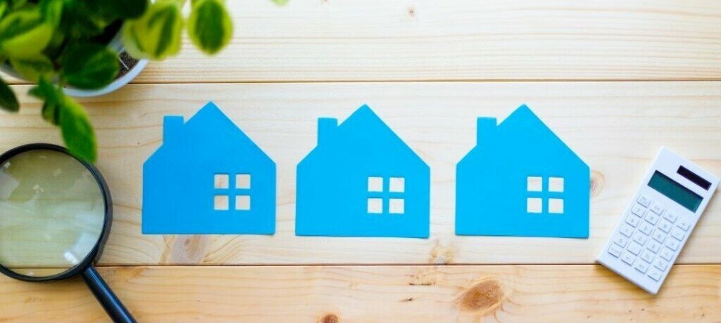 Blue paper cut outs of houses with a magnifying glass representing the Utah housing market.