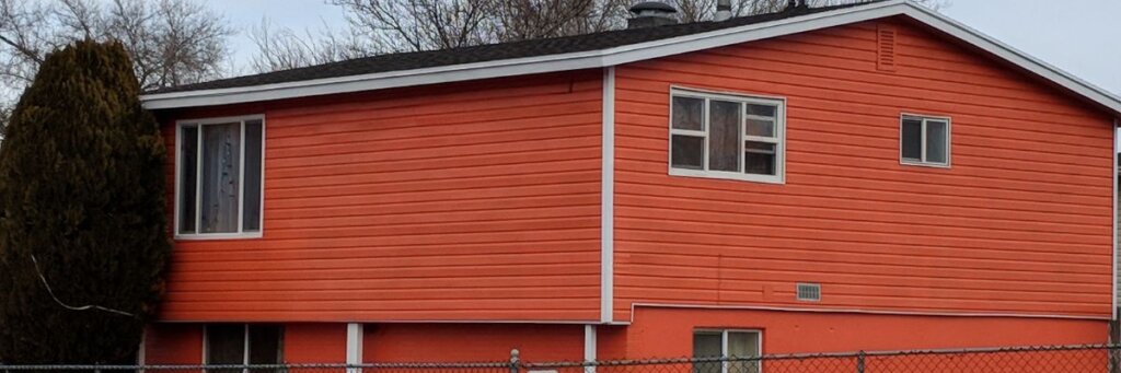 An orange house with a tall bush on the side.